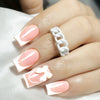 A hand displays white French style press-on nails with a coffin shape and a white chain ring.
