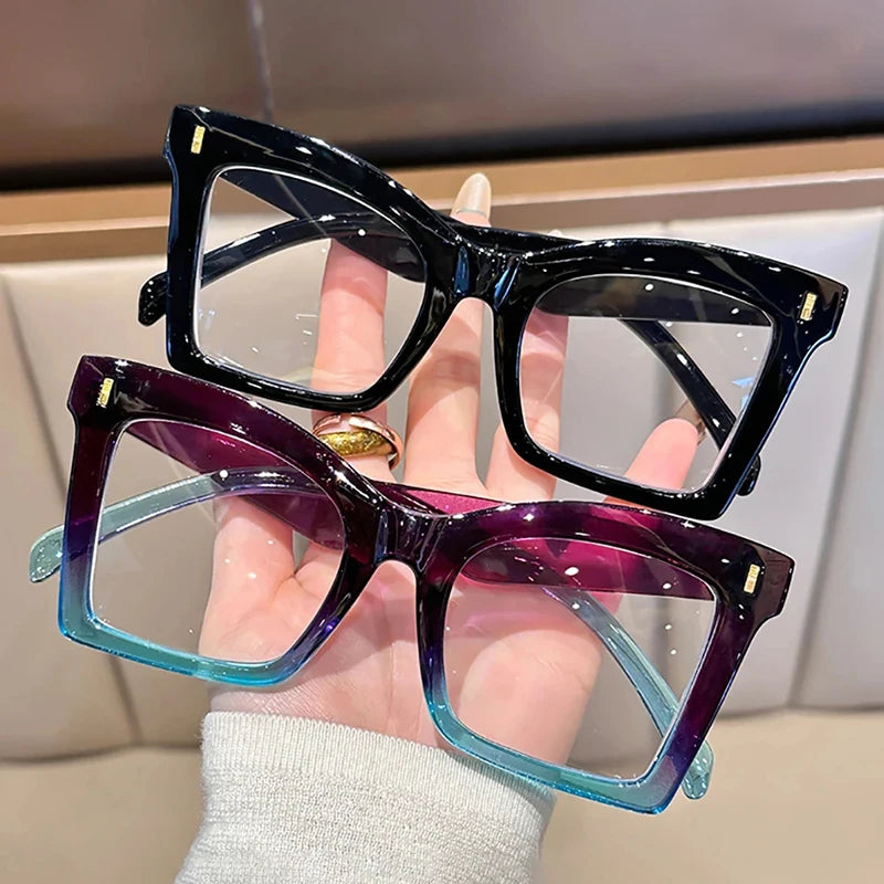 A hand holds a pair of square-framed reading glasses with purple and blue tinted lenses.