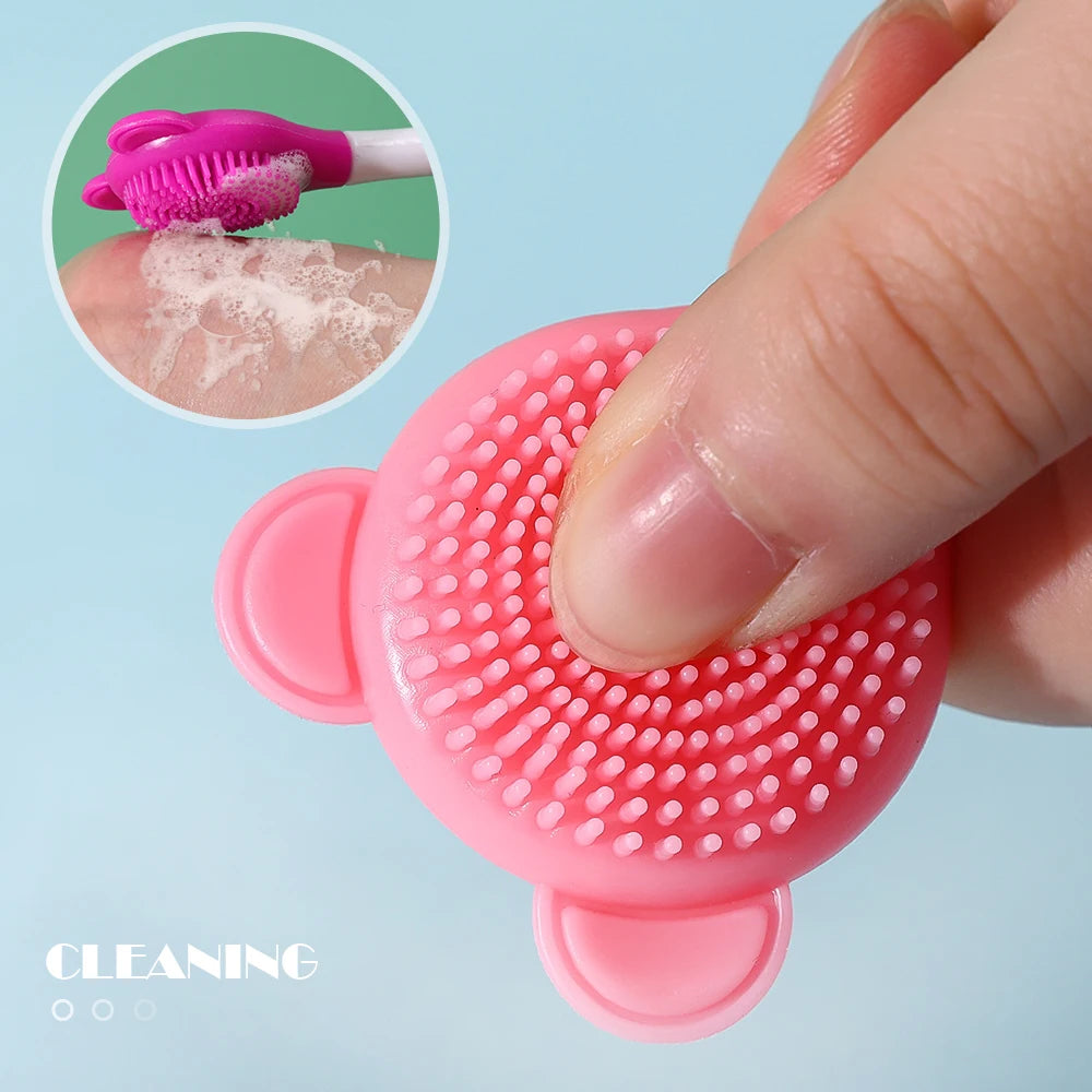 Una mano sostiene un cepillo de máscara facial de silicona rosa, con una vista ampliada mostrando espuma en las cerdas.
