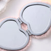 A heart-shaped foldable travel makeup mirror with a silver frame and pink fuzzy lining.