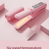 A pink portable dual-switch hair straightener and curler with a digital temperature display is shown on a light pink surface.