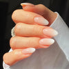 A hand displaying almond press-on nails with a pink bow design on the fingertips.