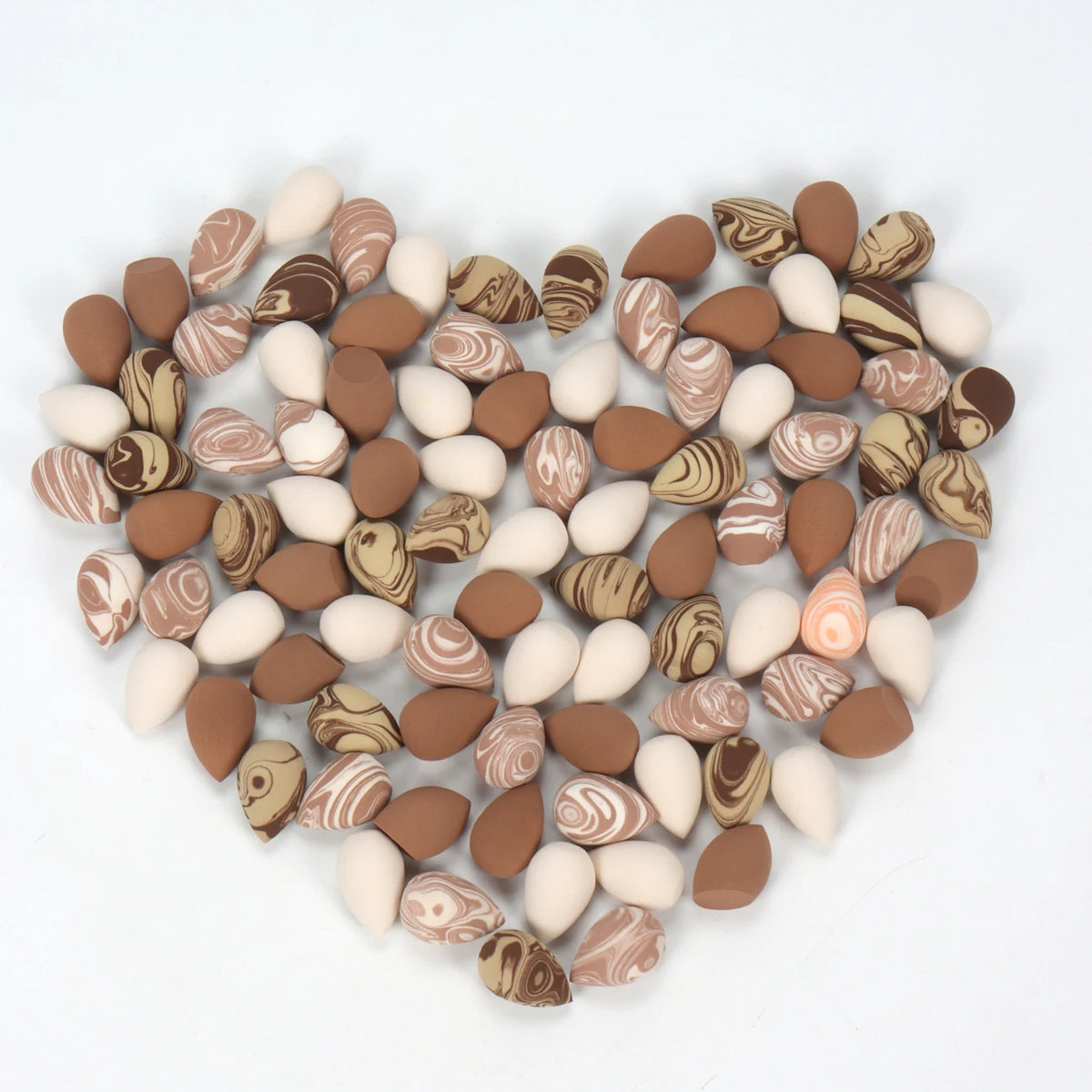 A heart-shaped arrangement of reusable expandable makeup sponges in various shades of brown, beige, and white.