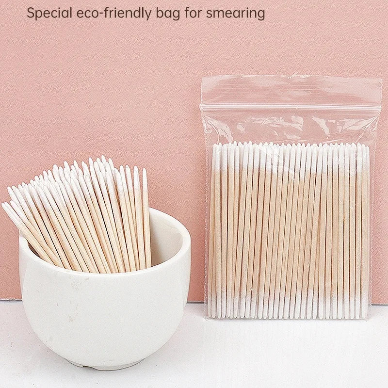 Un sac plastique transparent rempli de cotons-tiges blancs, à côté d'un bol en céramique contenant des cotons similaires.