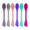 A row of six double head silicone face cleansing brushes in various pastel colors including purple, gray, pink, blue, and gre