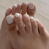 A close-up of a hand displaying a set of reusable press-on acrylic false nails painted in a pale milky white color.