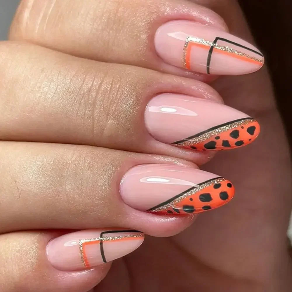 Close-up of a hand displaying press-on false nails with orange and black leopard print accents on a nude base.