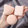 A hand holds three pink makeup sponge puffs, showing different shapes and textures.
