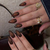 A close-up of a hand displaying pink flower almond press on nails with gold jewelry.