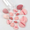 A collection of 15 pink makeup sponges and a clear bottle are arranged on a white surface.