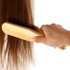 A hand is using a wooden double-sided hair comb to style long brown hair.
