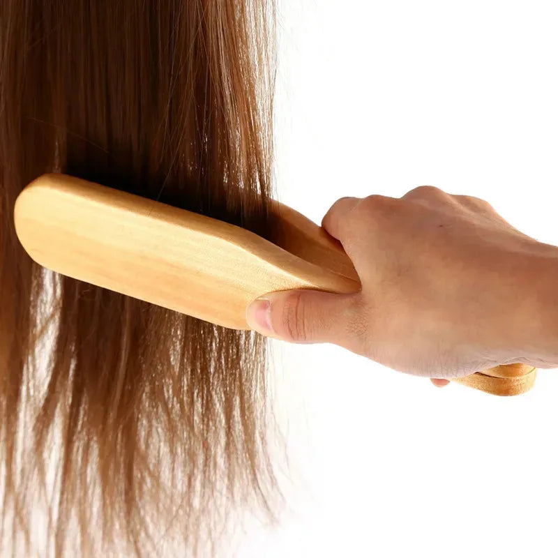 A hand is using a wooden double-sided hair comb to style long brown hair.