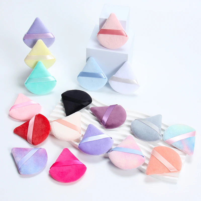 Une collection de six éponges de maquillage triangulaires dans différentes nuances de rose, violet et vert, arrangées sur une