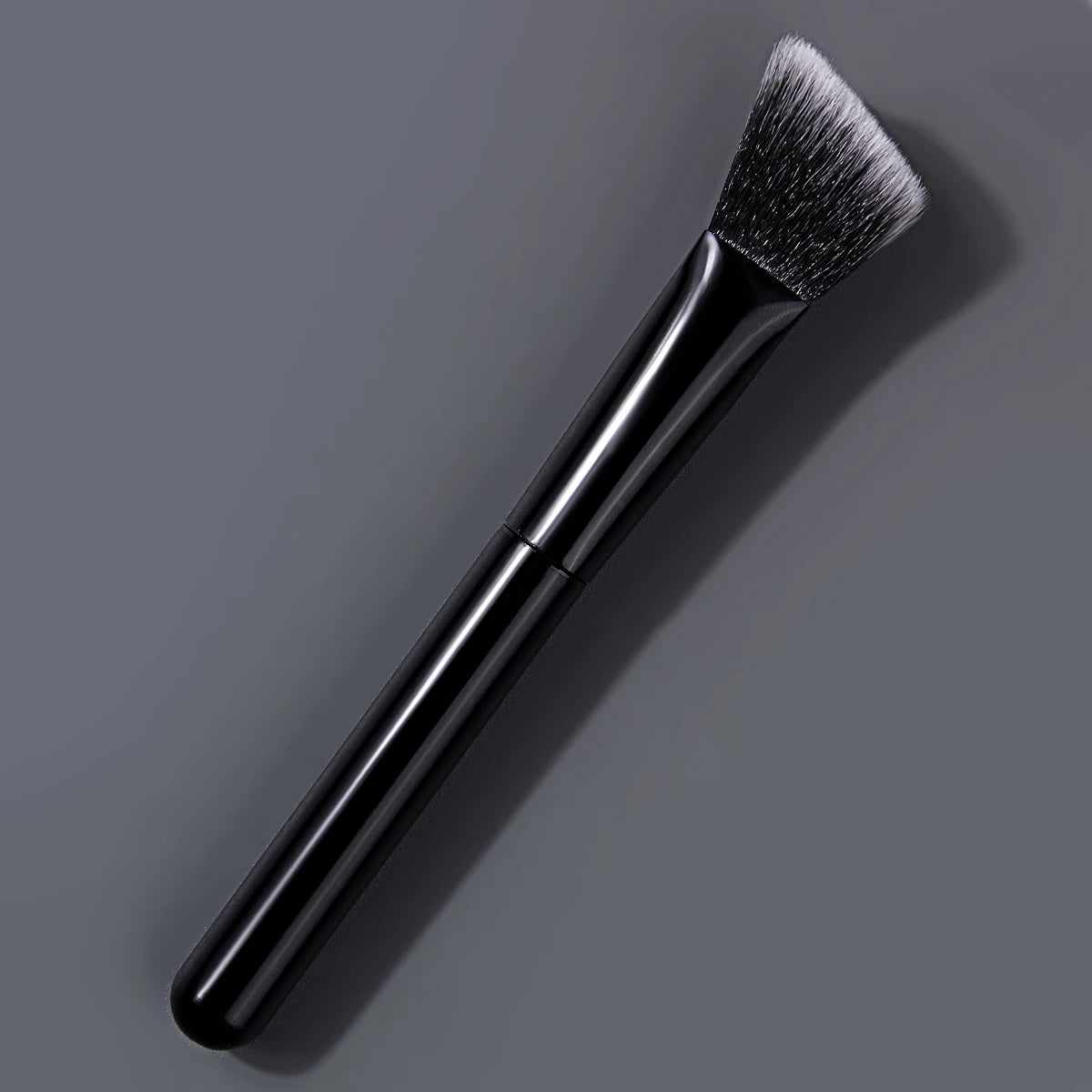 A black triangular precision concealer brush shown against a gray background.