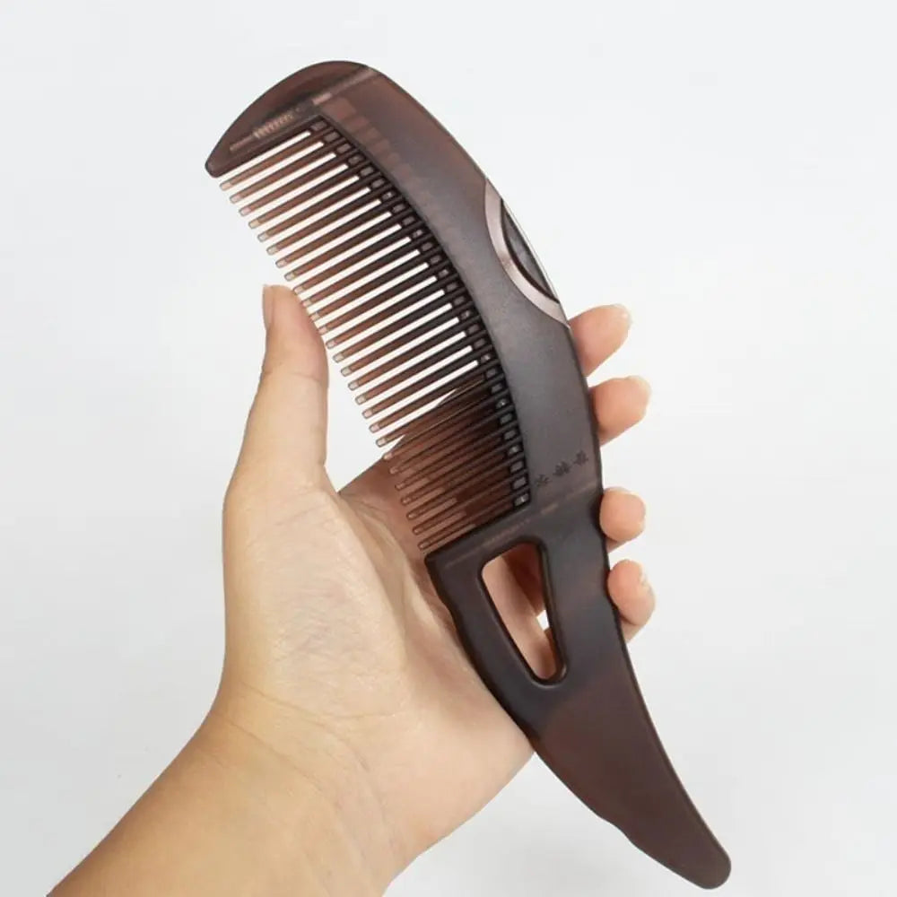 Eine Hand hält eine dunkle braune hohle Anti-Haarausfall-Massagebürste mit feinen Zähnen.