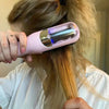 A hand holds a pink cordless hair clipper with a purple-tinted blade against a person's blonde hair.