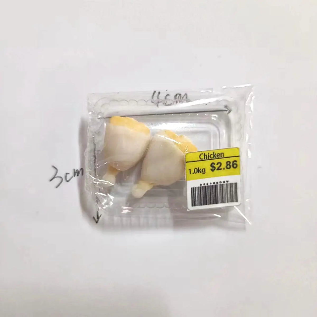 Un emballage plastique transparent contenant deux pièces de simulation de nourriture en forme de poulet pour maisons de poupé