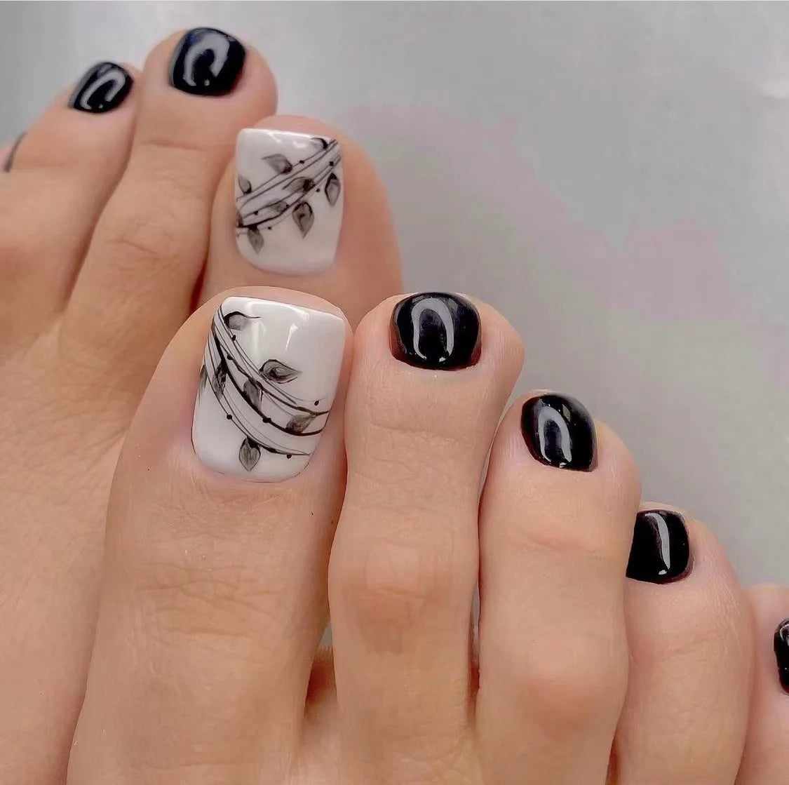 Nahaufnahme einer Hand, die wiederverwendbare falsche Zehennägel mit schwarz-weißen Blattmotiven zeigt.