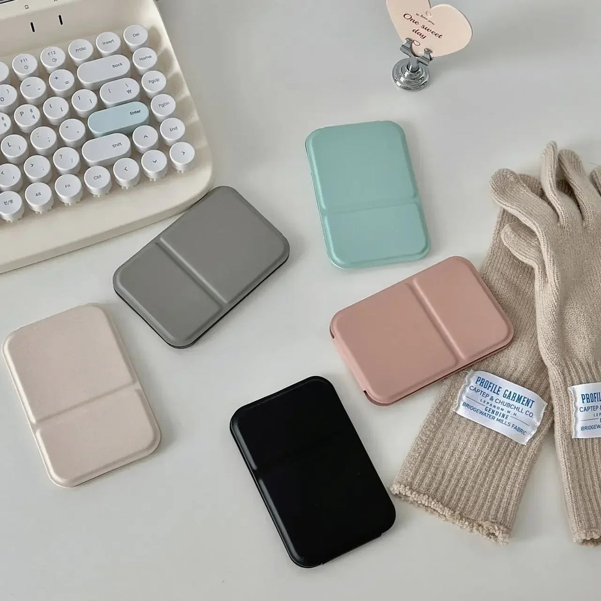 A collection of portable makeup mirrors in various colors and a silicone makeup brush is displayed on a white surface.