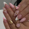 A close-up of hands displaying 24-piece almond press-on nails with delicate pink and white floral designs.
