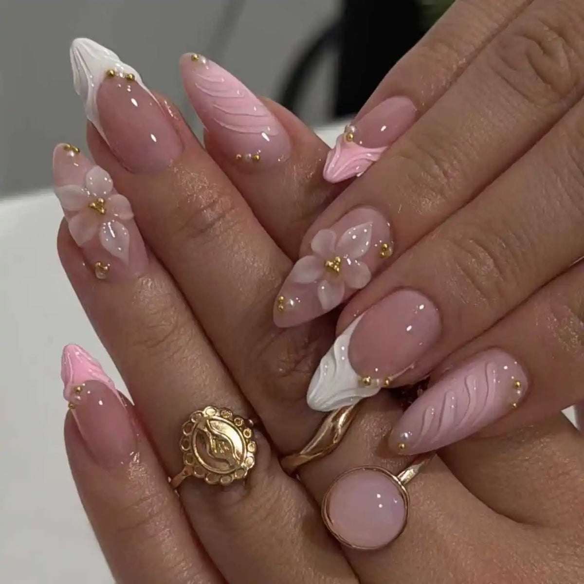 A close-up of hands displaying 24-piece almond press-on nails with delicate pink and white floral designs.