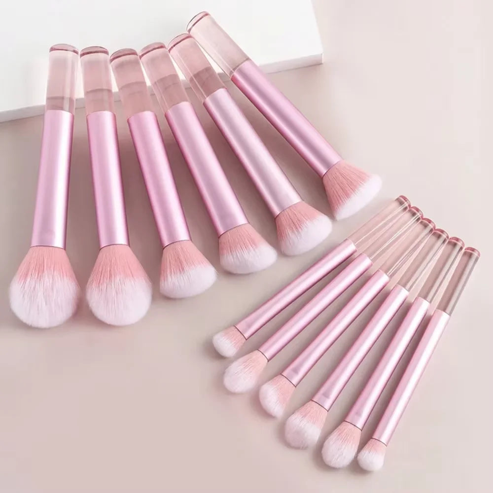 Un juego de doce brochas de maquillaje profesionales de color rosa suave dispuestas sobre un fondo claro.