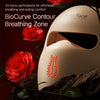 A beige light therapy mask with micro-perforations is shown next to red roses and dark wood.