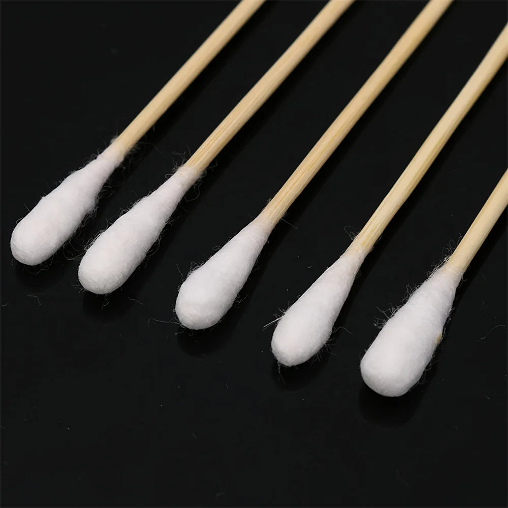Plusieurs cotons-tiges à manche en bois avec des extrémités en coton blanc, présentés sur fond noir.