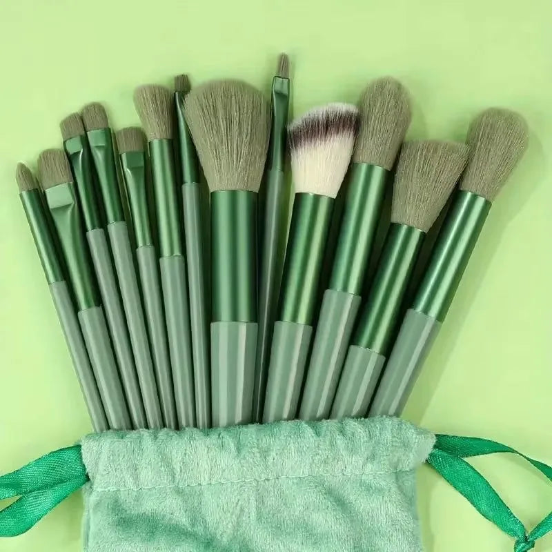 A set of thirteen professional makeup brushes with green and gray handles resting in a light green fabric pouch.