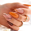 A hand displays press-on false nails with an orange and nude French wavy design on several fingers.