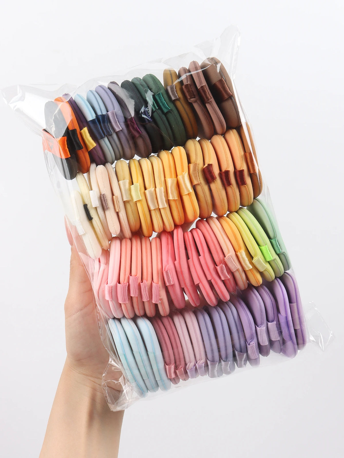 A hand holds a clear plastic bag filled with a variety of colorful beauty puffs and air cushions.