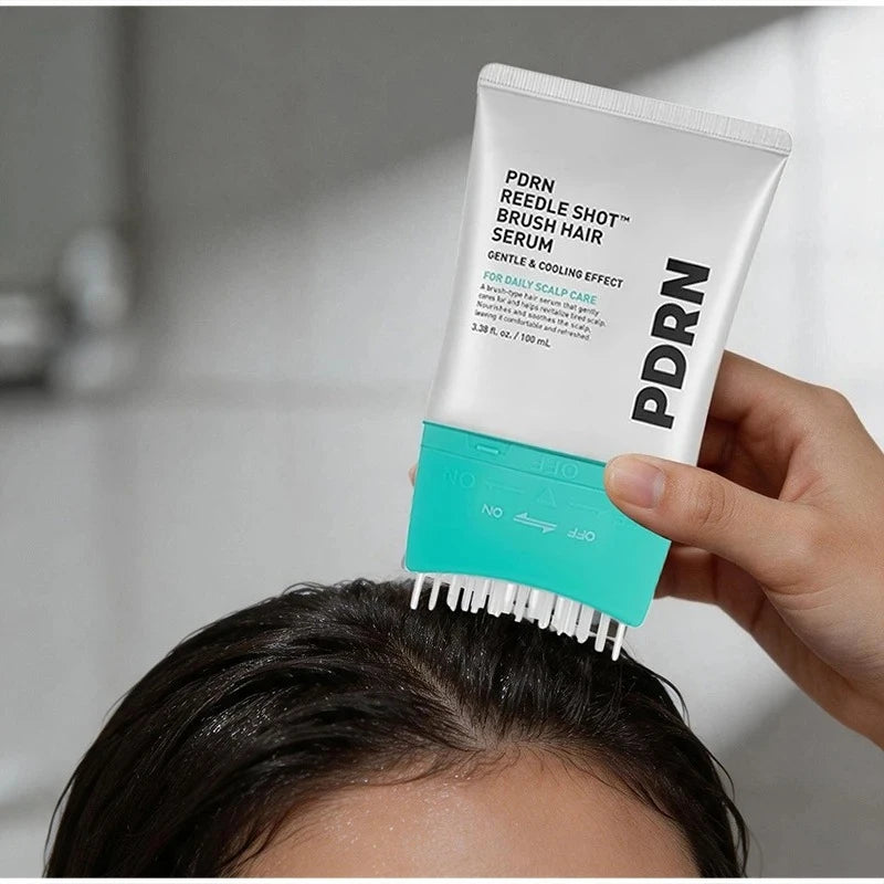 A hand holds a tube of PDRN Reedle Shot Brush Hair Serum for daily scalp care, with the brush head positioned on a person's h