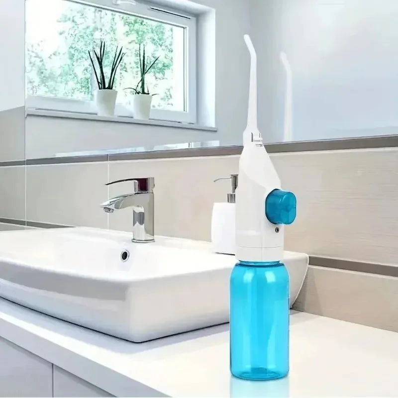 A manual high-pressure dental flosser in white and blue sits on a white bathroom counter next to a sink.