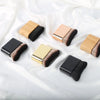 A collection of five makeup brushes with wooden and black handles and gold accents displayed on white fabric.