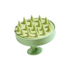 A light green scalp massage brush with numerous pointed protrusions for relaxation.