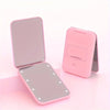 A pink mini folding makeup mirror with an open and closed view, shown on a light surface.