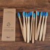 A set of ten natural bamboo toothbrushes packaged in a cardboard box on a wooden surface.