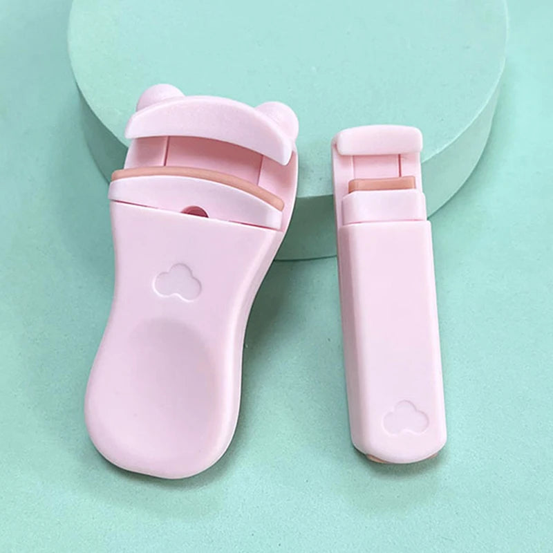 A pink cartoon mini eyelash curler is shown on a light green background.