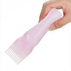 A hand is holding a pink hair color applicator bottle with a fine-tooth comb attached.
