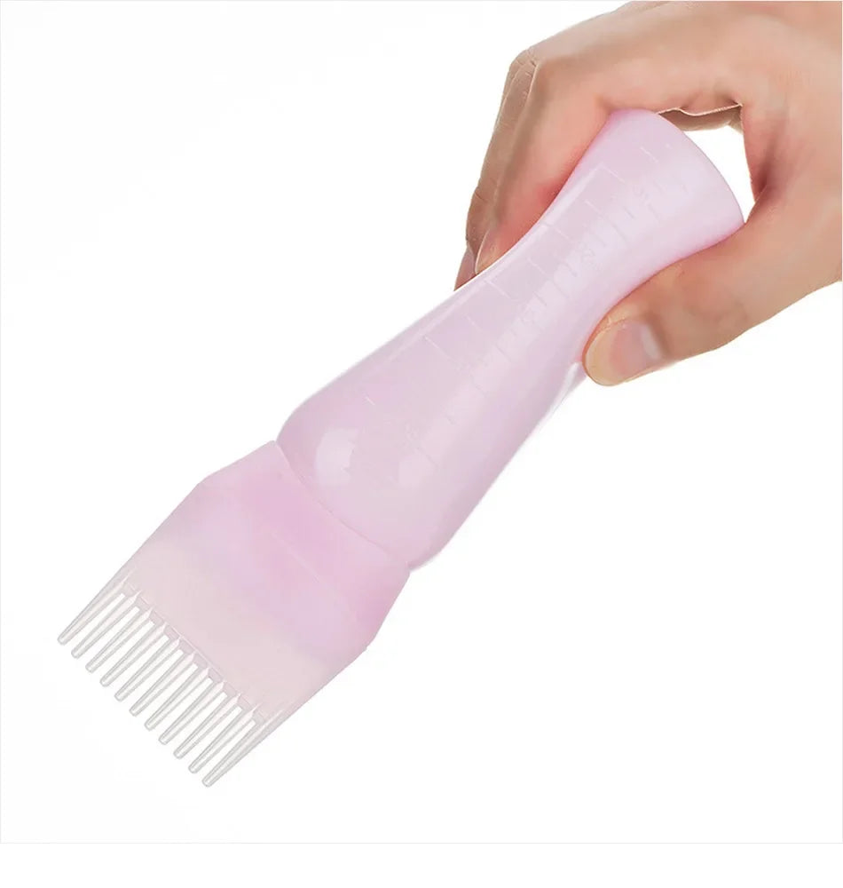 A hand is holding a pink hair color applicator bottle with a fine-tooth comb attached.