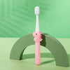 A pink dinosaur-themed toothbrush with white bristles is displayed on a green wooden arch.