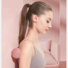 A woman with long hair tied in a ponytail is shown relaxing, holding a pink deep tissue massage ball.