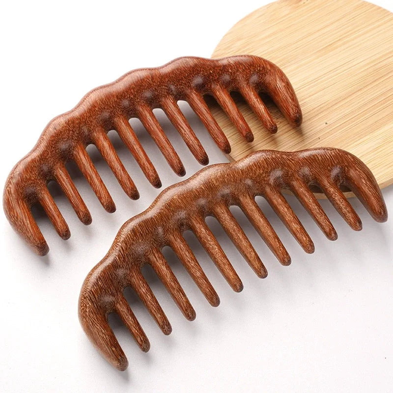 A pair of natural golden sandalwood wide-tooth detangling combs resting on a light wooden board.