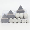 A set of twelve all-purpose makeup sponges in gray and white shades arranged on a white surface.