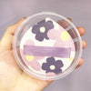A makeup puff set featuring pink and purple floral designs is shown inside a clear storage box.