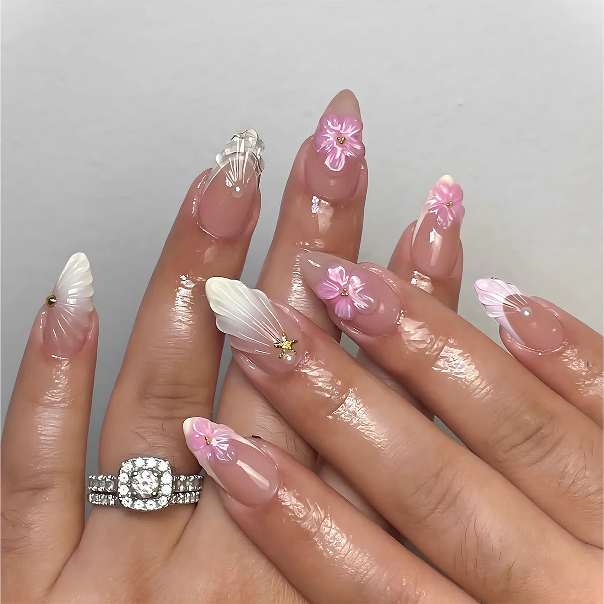 A hand displays a set of 24-piece almond press-on nails featuring pink and white floral and butterfly designs.