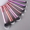 A set of seven professional makeup brushes with metallic pink and purple handles and fluffy bristles arranged diagonally.