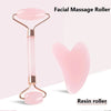 A pink resin facial massage roller with a gold-toned handle and heart-shaped stone.