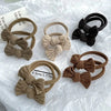 Colección de diez gomas para el pelo de trenzas de tejido beige y negro, mostradas en papel blanco.