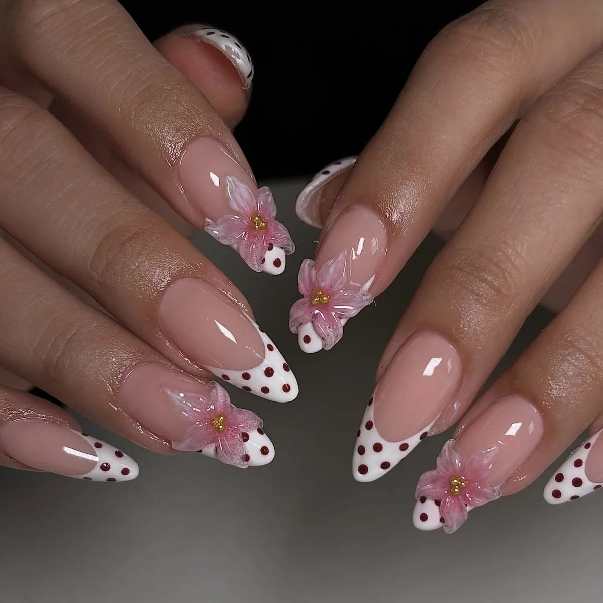 A close-up of hands displaying pink flower press on nails with white tips and accents.